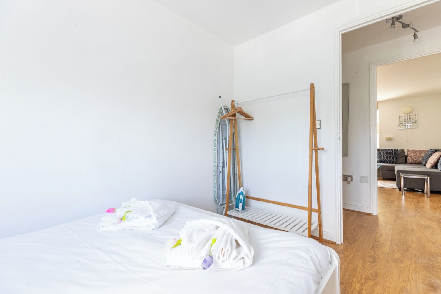 A bedroom with a bed, a hanging clothes rack, and a wooden floor.