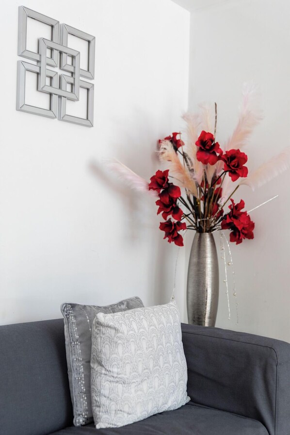 Un salon moderne avec un canapé gris, un vase décoratif orné de fleurs rouges et une œuvre d’art géométrique accrochée au mur.