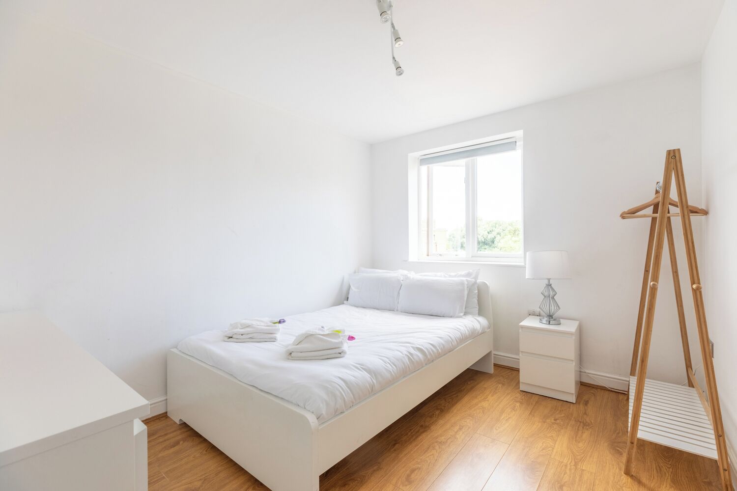 Een minimalistische slaapkamer met een bed, nachtkastjes, een raam en een houten trap.