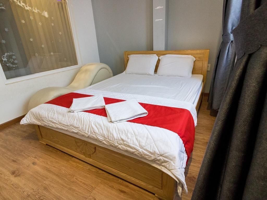 Una cama bien hecha con una colcha roja y blanca, un cabecero de madera y una ventana con persianas.