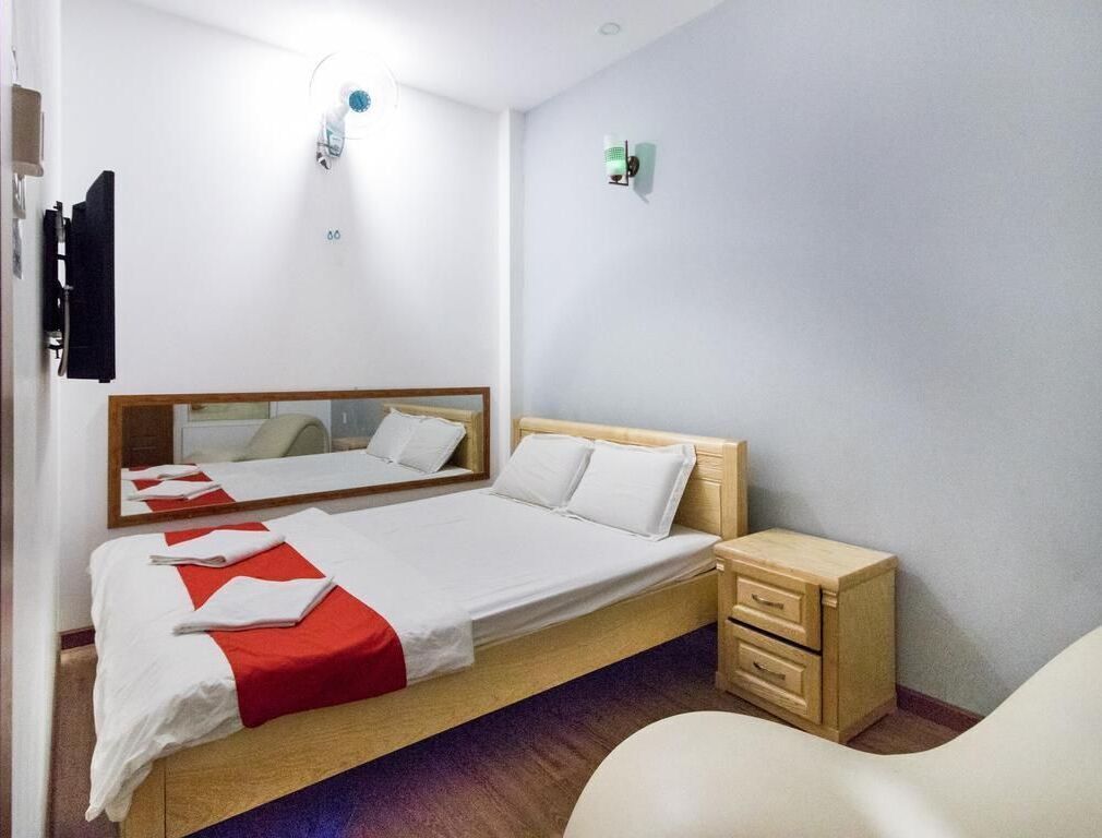 A hotel room with a bed, bedside table, and a mirror.