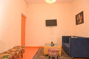 A living room with a sofa, a small table with a plant, a bench, and a television mounted on the wall.