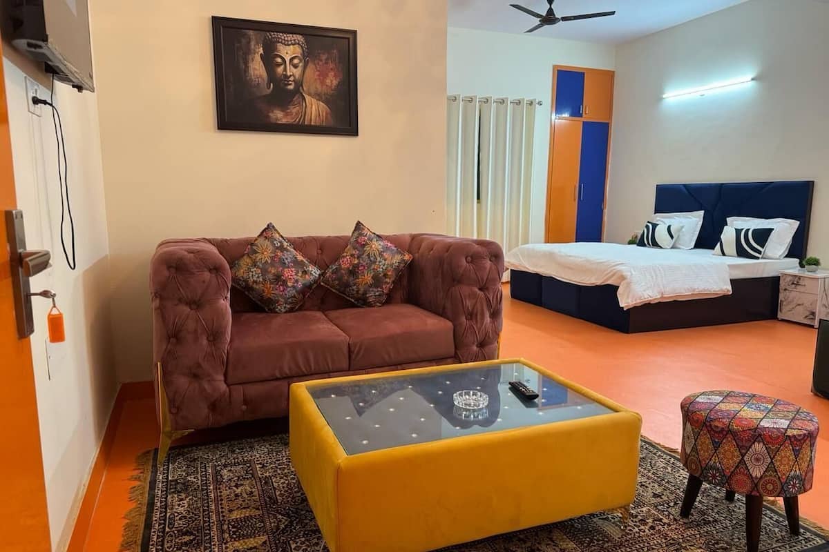 A modern room with a sofa, a glass coffee table, a patterned rug, a bed, and a ceiling fan.