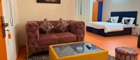 A modern room with a sofa, a glass coffee table, a patterned rug, a bed, and a ceiling fan.