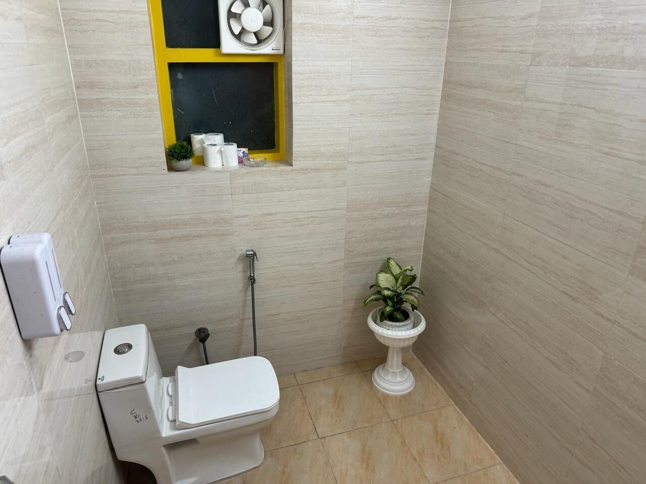 Un bagno moderno e compatto con toilette, bidet, lavandino, una ventola e una pianta in vaso.