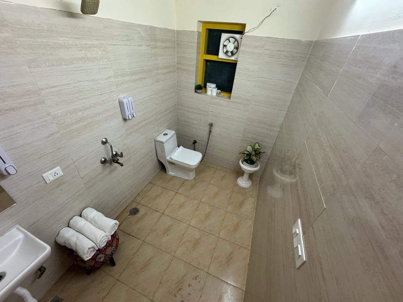 Une petite salle de bain avec des toilettes, un lavabo et une petite fenêtre équipée d’un ventilateur.