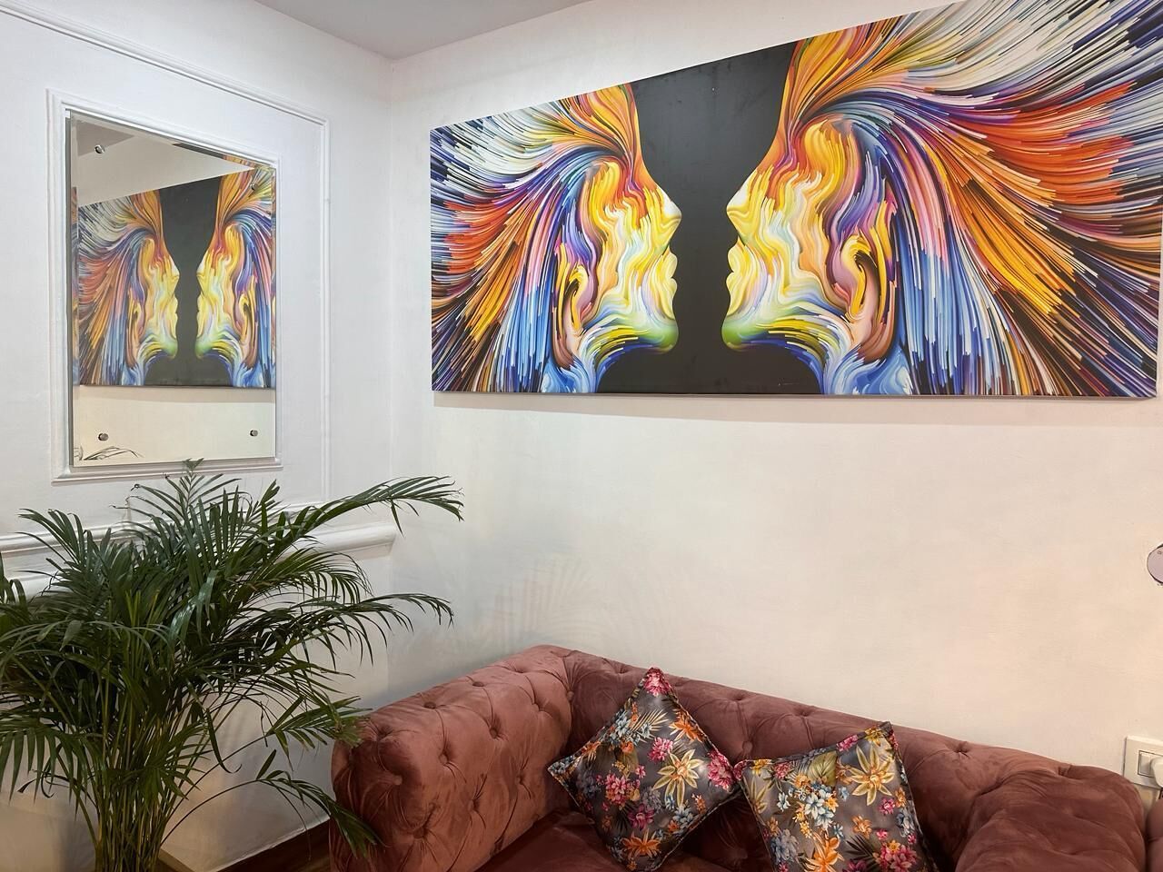 A living room with a large abstract painting, a brown sofa, and a potted plant.