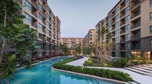 A modern residential building with a central swimming pool, surrounded by lush greenery and well-maintained landscaping.