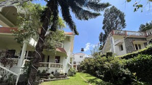 A courtyard with a tree, a table, and a pathway leading to a building with balconies. - Le Hayat 4Bhk Pvt-Villa Kodaikanal TN (Kodaikanal)