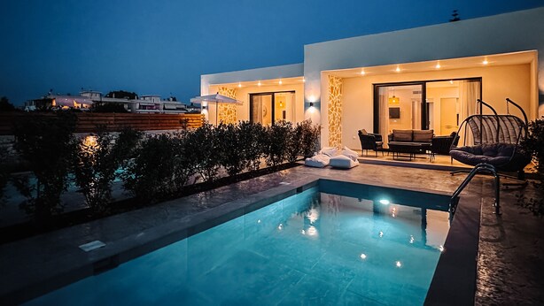 A modern poolside area with a clear pool, outdoor seating, and a well-lit entrance. - Melior Luxury Villas Preveza (Preveza)