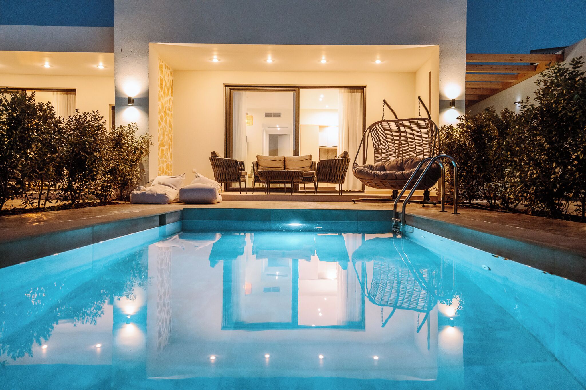 A swimming pool with a sunken seating area, surrounded by a patio with a table and chairs, and a hanging chair.