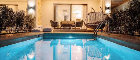 A swimming pool with a sunken seating area, surrounded by a patio with a table and chairs, and a hanging chair.