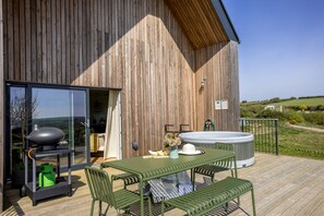 A wooden building with a patio area featuring a table and chairs, a barbecue grill, and a hot tub. - 3 The Vista, Willingcott Nr Woolacombe - Hot tub/ Pet friendly/ On-site pool/ EV Charger/ Ecohome (Woolacombe)