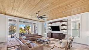 A spacious living room with a wooden ceiling, large windows, a flat-screen TV, and a dining area. - Crystal Del Mar. New! Private Pool, Gulf Views (Destin)