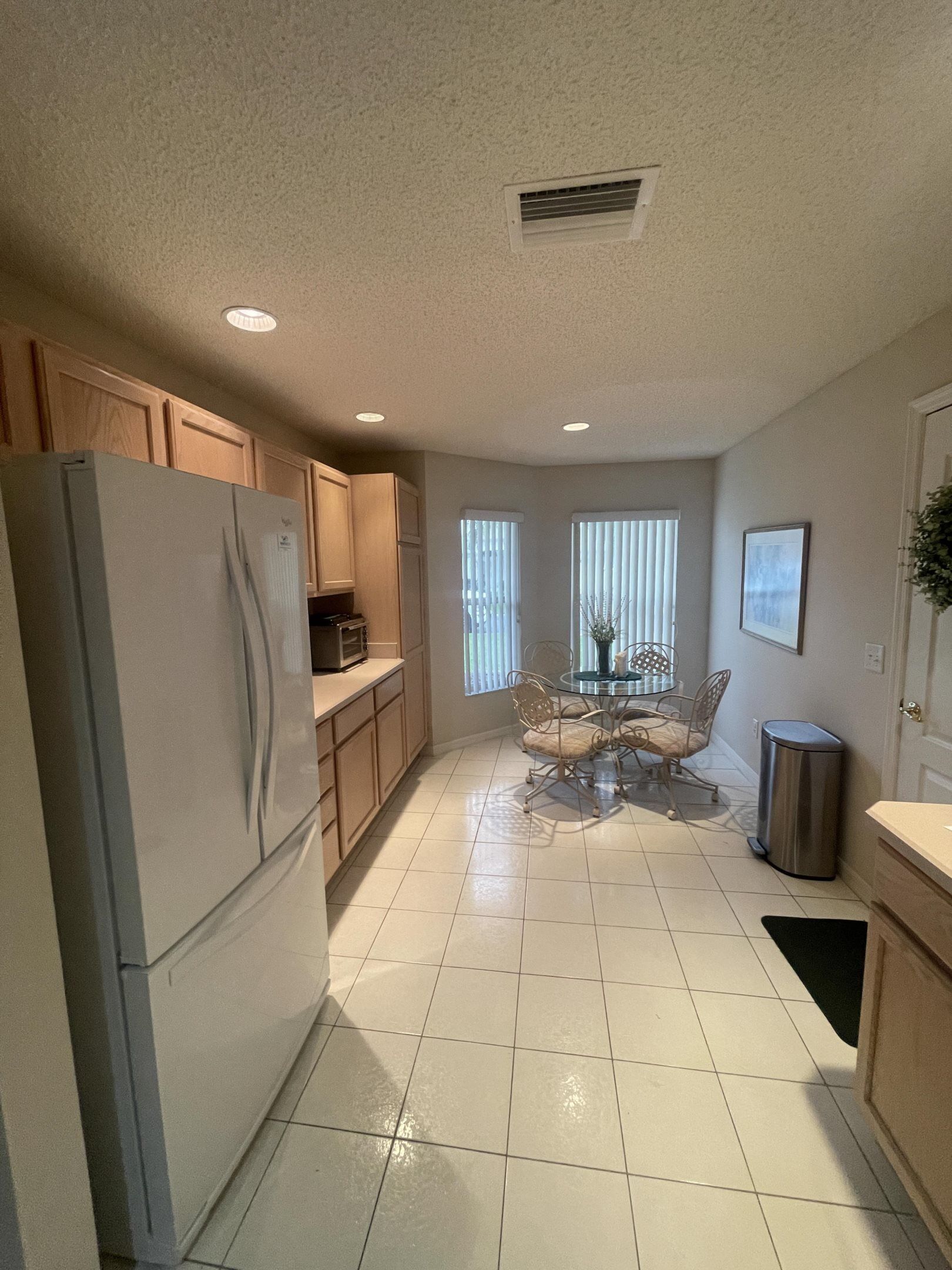 A kitchen with a refrigerator, cabinets, a dining table with chairs, and a trash can.