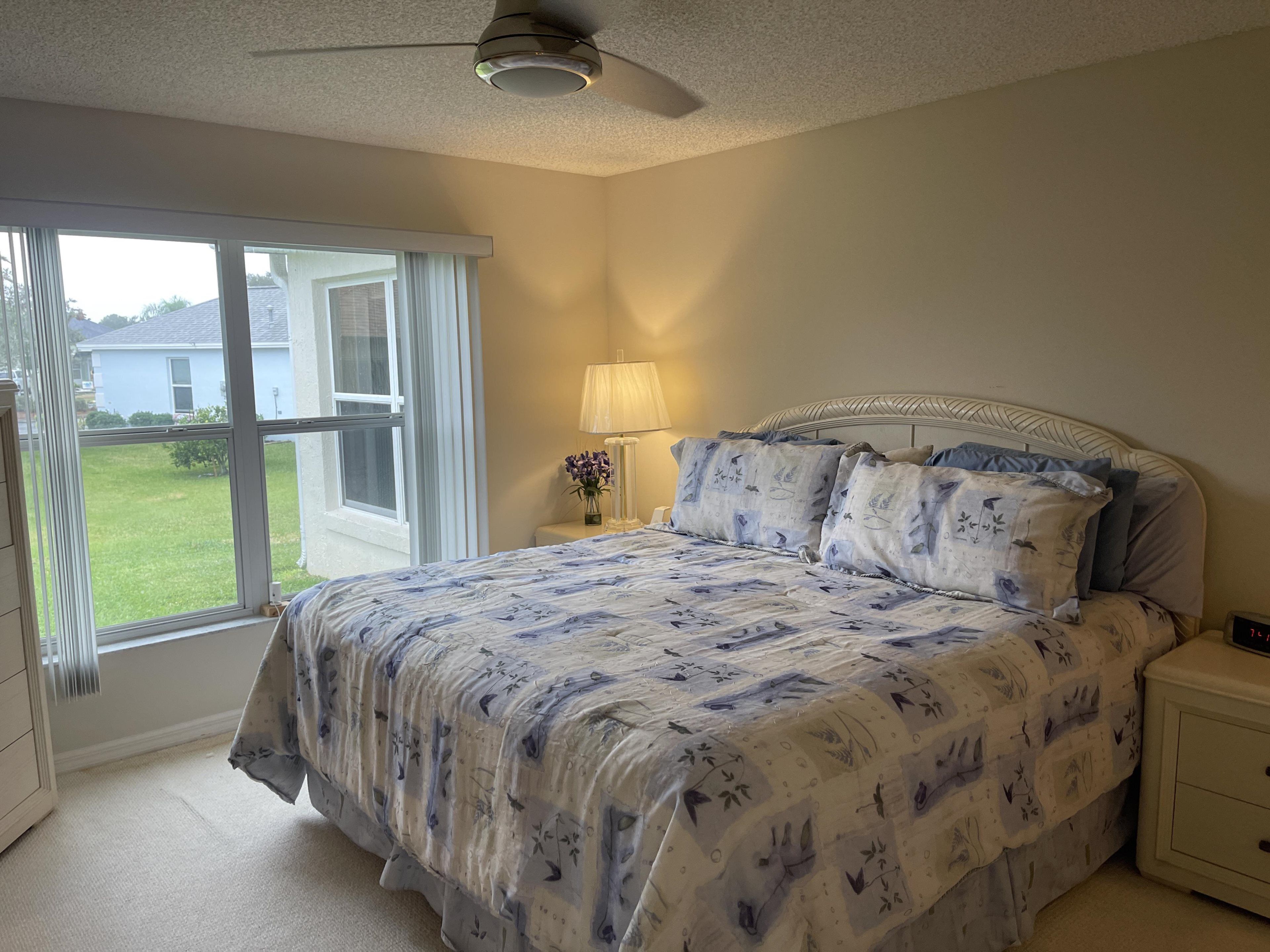 A bedroom with a large bed, a nightstand, a lamp, and a ceiling fan.