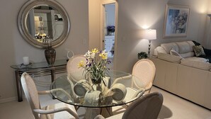 Un coin repas avec une table en verre et des chaises en osier, un canapé, une lampe et un tableau au mur.