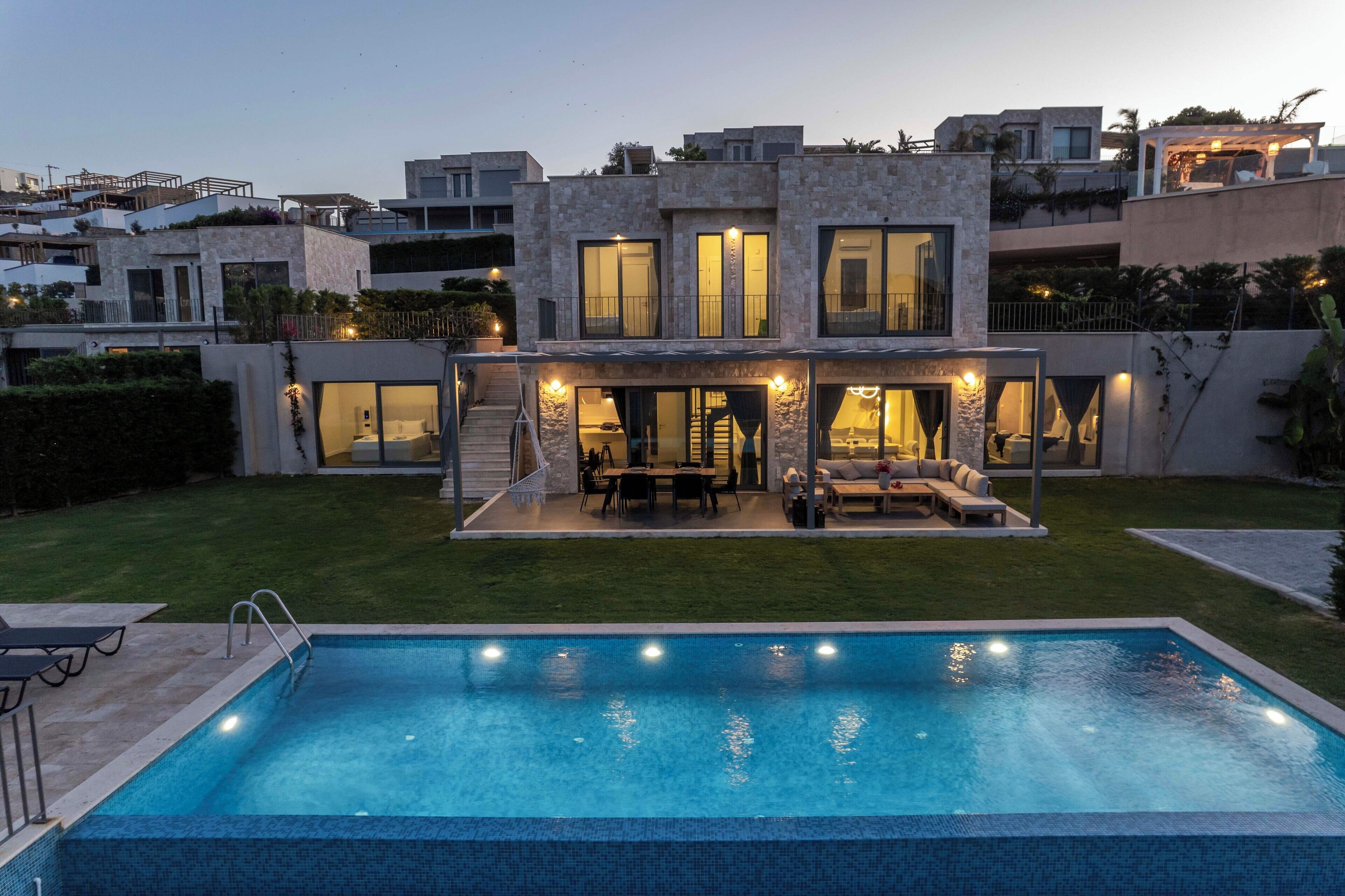 A modern two-story house with a swimming pool, outdoor seating, and a well-maintained lawn.