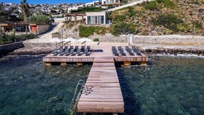 A wooden pier leading to a beach with clear water, surrounded by a hillside with houses. - Bovilla Hotels Salt Yalikavak (Bodrum)