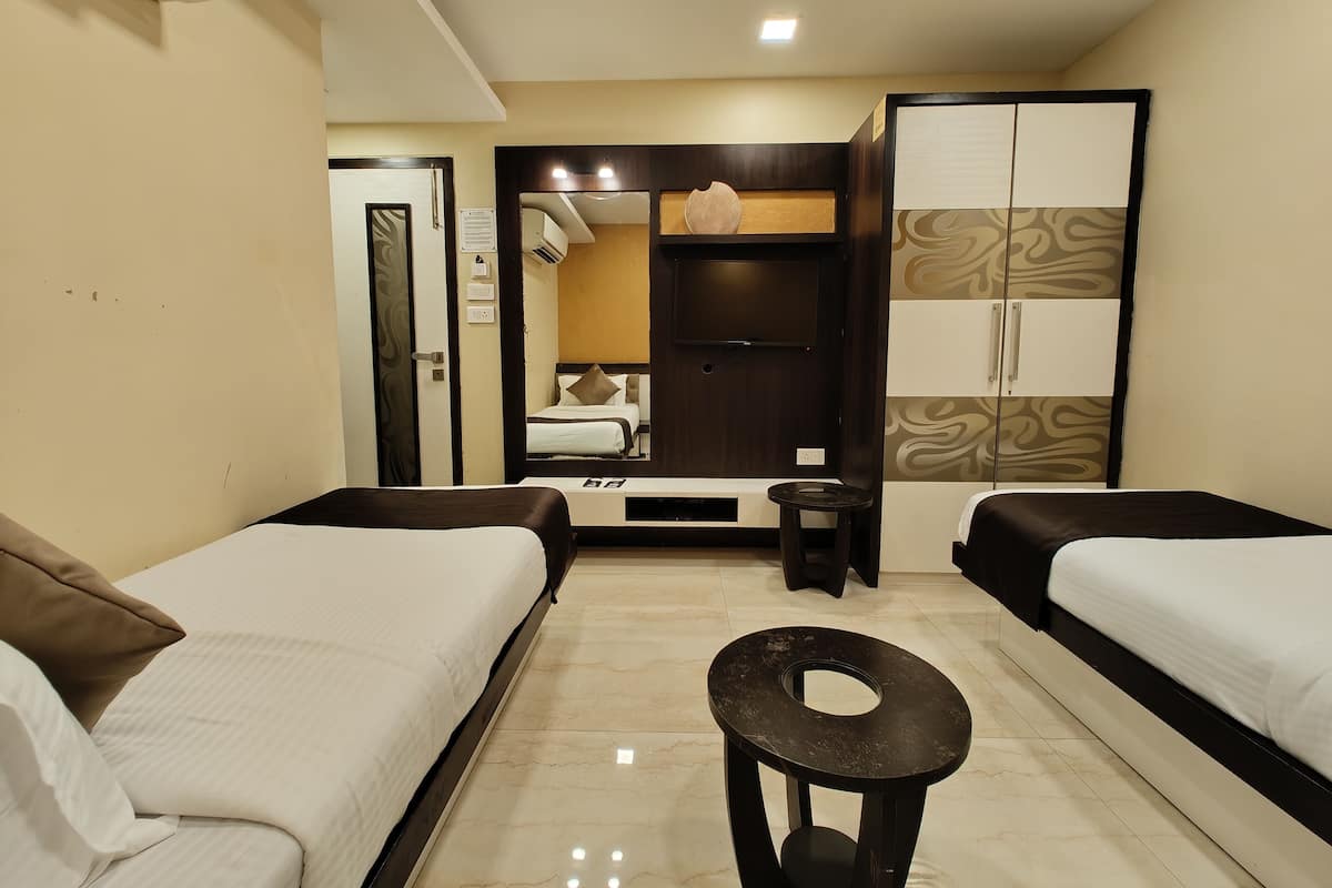 A hotel room with two beds, a small round table, a wardrobe, and a mirror.