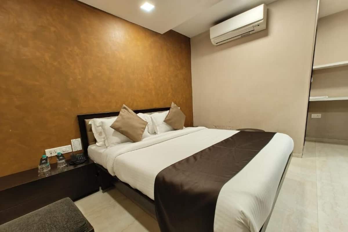A hotel room with a bed, bedside table, and an air conditioning unit.