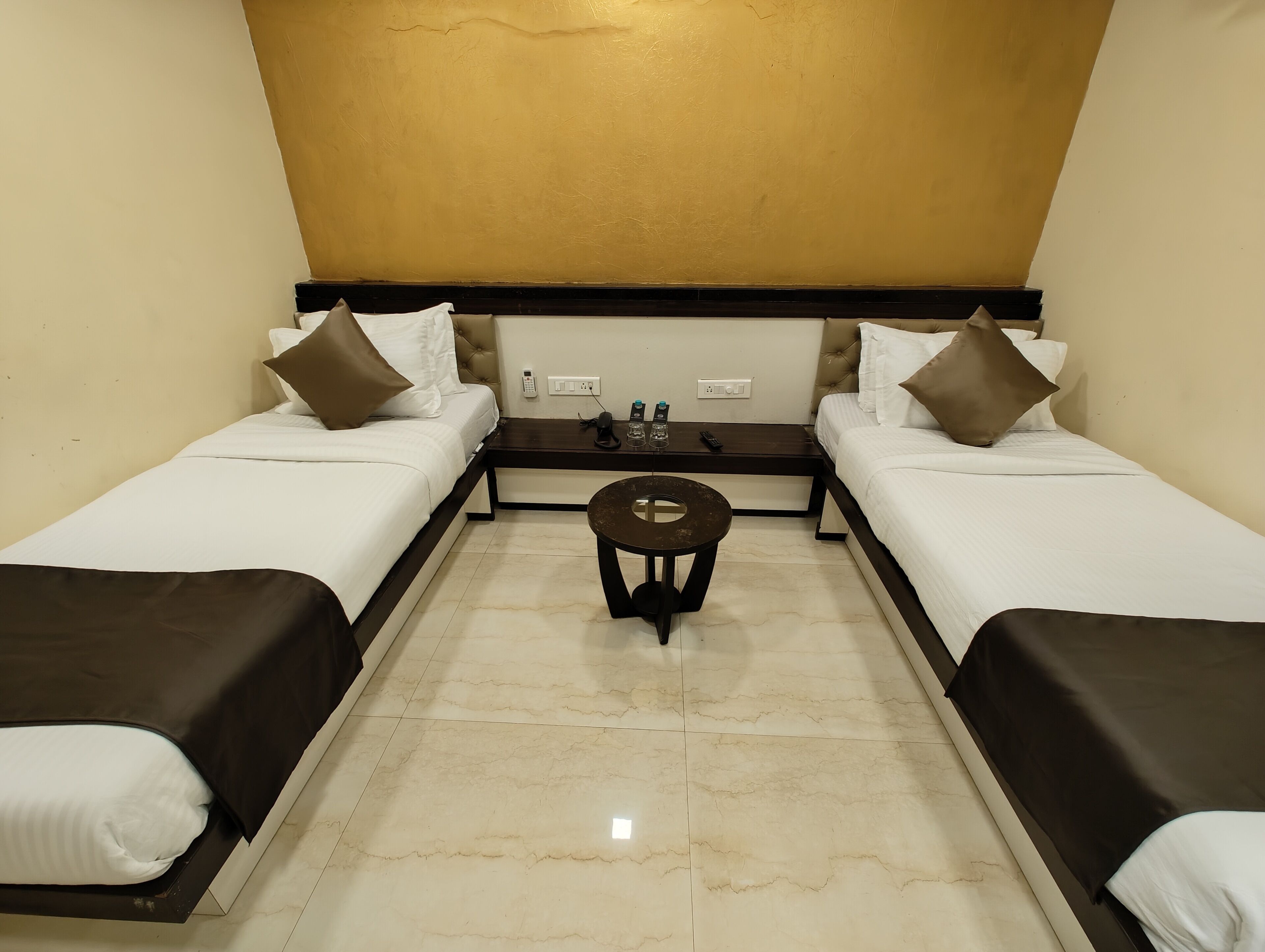 A hotel room with two single beds, a small round table, and a wall-mounted phone.