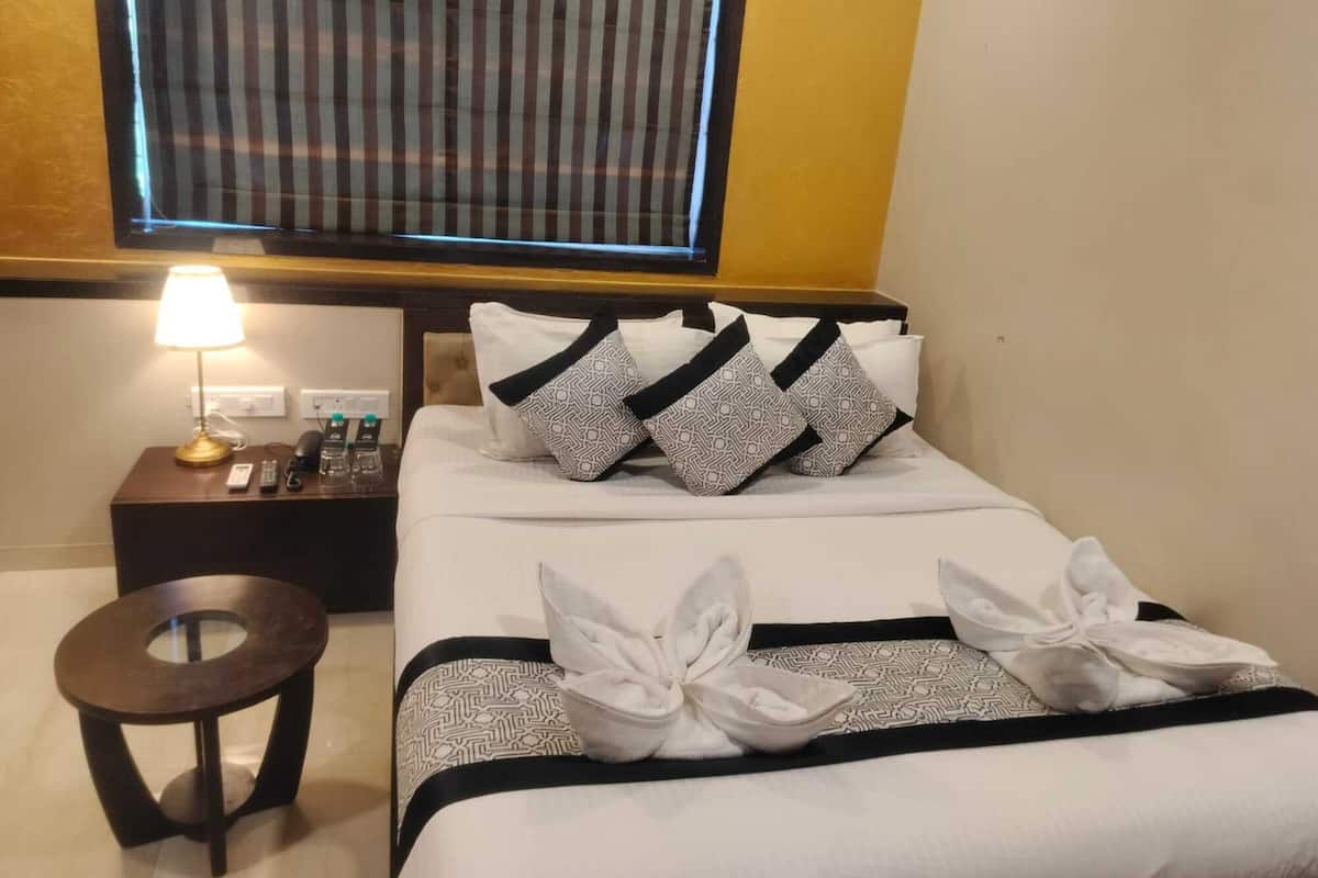 A hotel room with a bed, a bedside table with a lamp, a small round table, and a window with blinds.