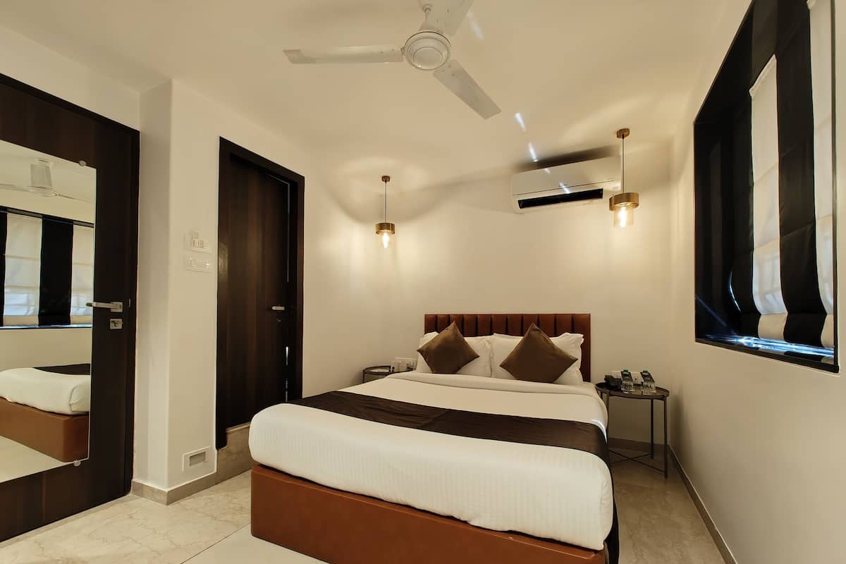 A modern hotel room with a large bed, a ceiling fan, an air conditioning unit, a bedside table with a lamp, and a large mirror.
