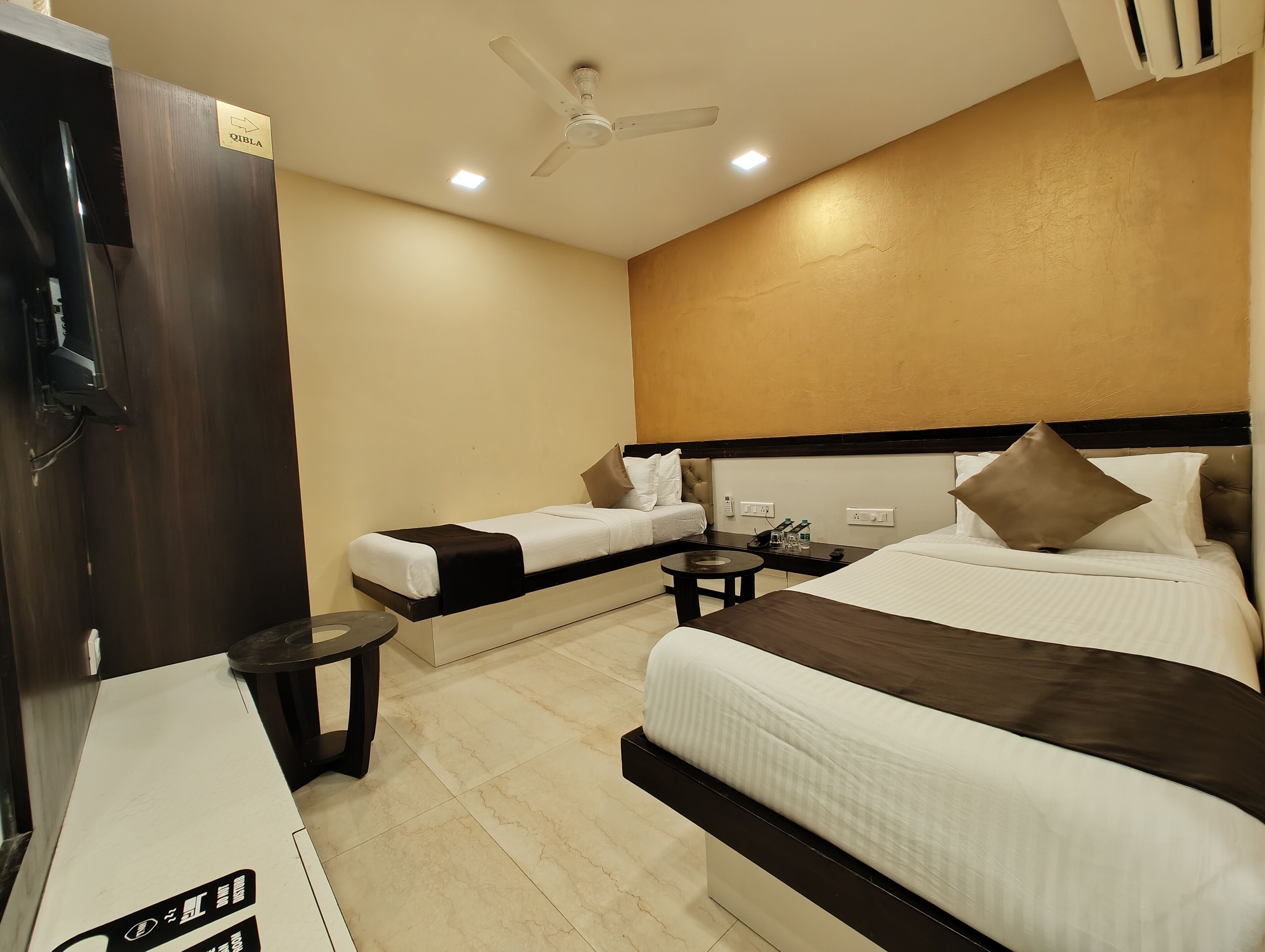 Habitación de hotel con dos camas, un escritorio, una silla, una mesita, un ventilador de techo y un mini bar.