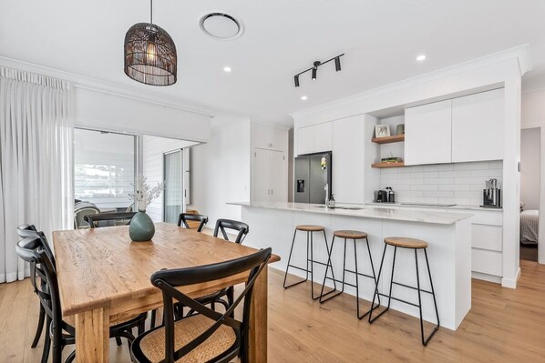 A modern kitchen with white cabinetry, a central island with stools, and a dining area with a wooden table and chairs.