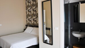 Ein Hotelzimmer mit Bett, Spiegel, Bad mit Waschbecken und Dusche.