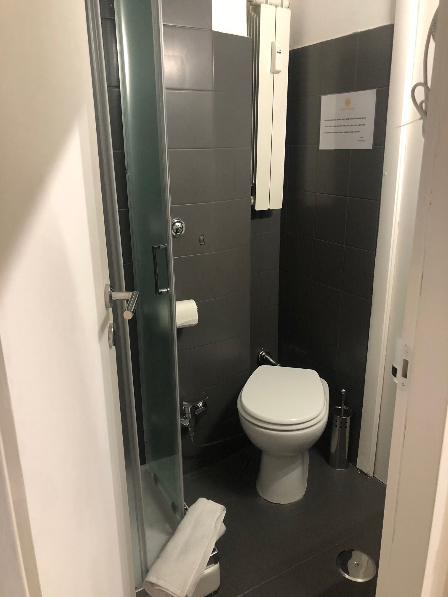 Un bany petit i funcional amb vàter, box de dutxa de vidre i paraigua per a tovalloles.