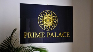 Ein Schild mit einem sonnenähnlichen Logo und dem Schriftzug 'PRIME PALACE' vor dunklem Hintergrund.