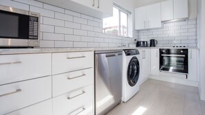 Eine moderne Küche mit weißen Schränken, einer Edelstahl-Mikrowelle, einer Waschmaschine und einem Backofen.