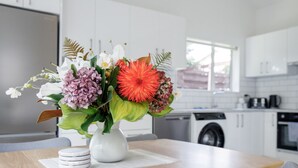 Eine moderne Küche mit weißen Schränken, einem Edelstahlkühlschrank und einem Essbereich mit einem Holztisch und einer Blumenvase.