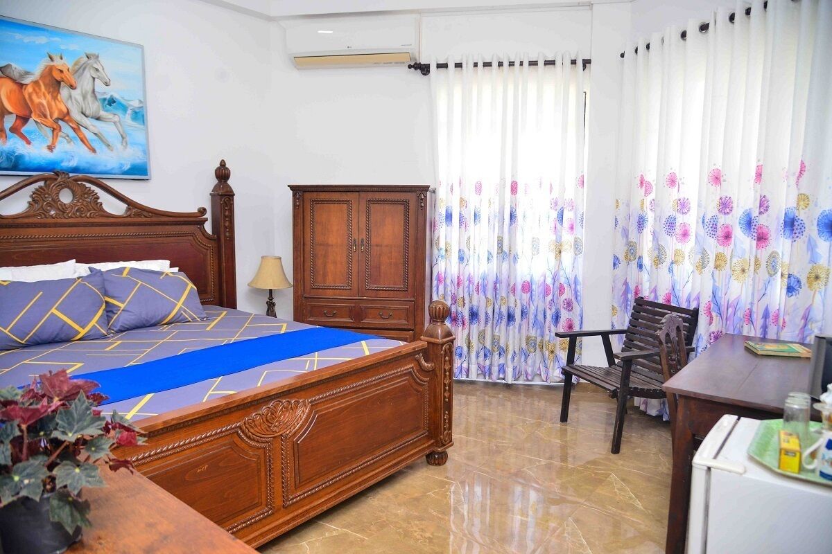 A bedroom with a wooden bed, a desk, a chair, a wardrobe, and a painting on the wall.