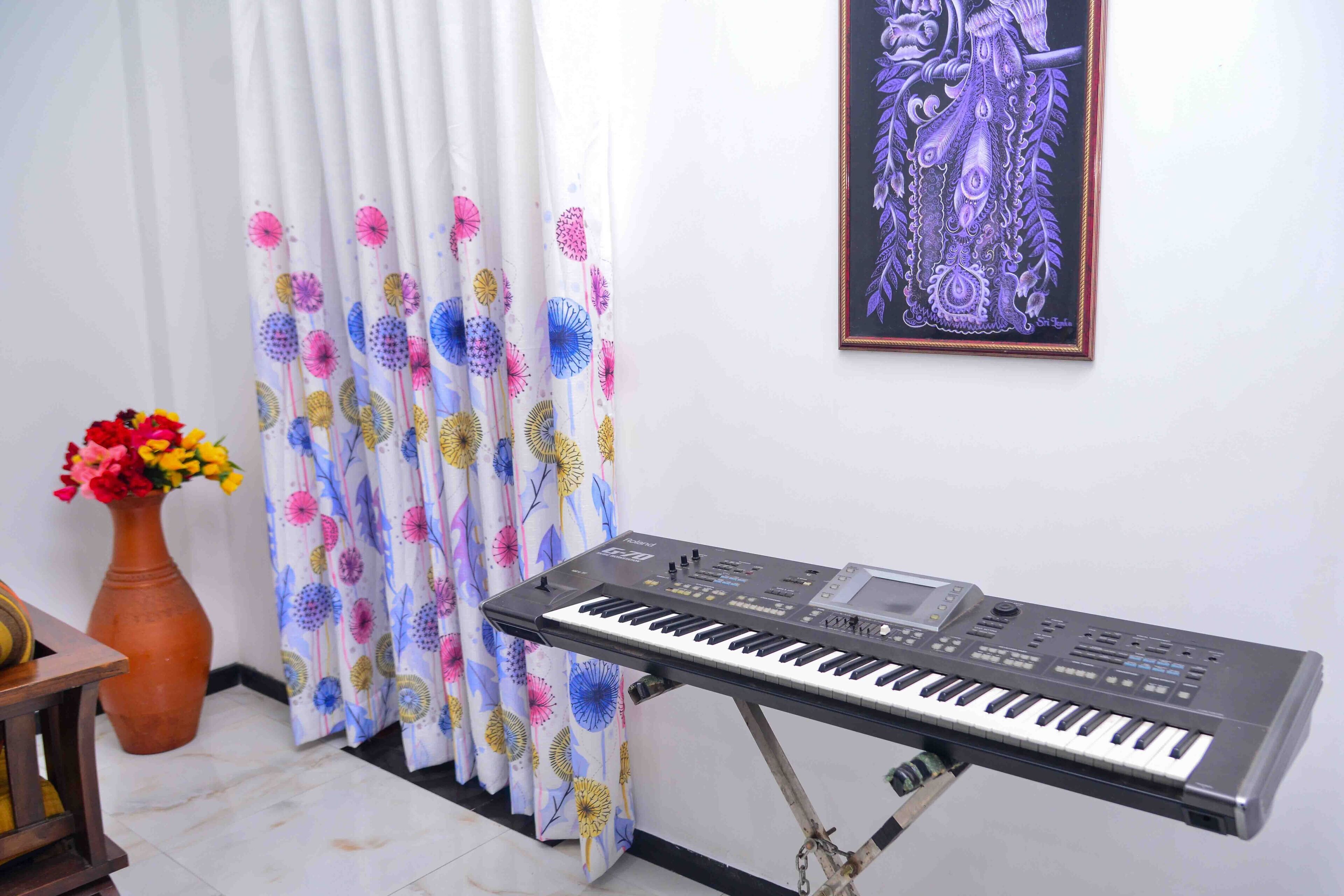 A keyboard on a stand in a room with a curtain and a vase of flowers.