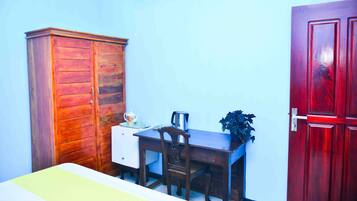 Een kamer met een houten garderobe, een bureau met stoel, een kleine tafel met een plant, en een rode deur.