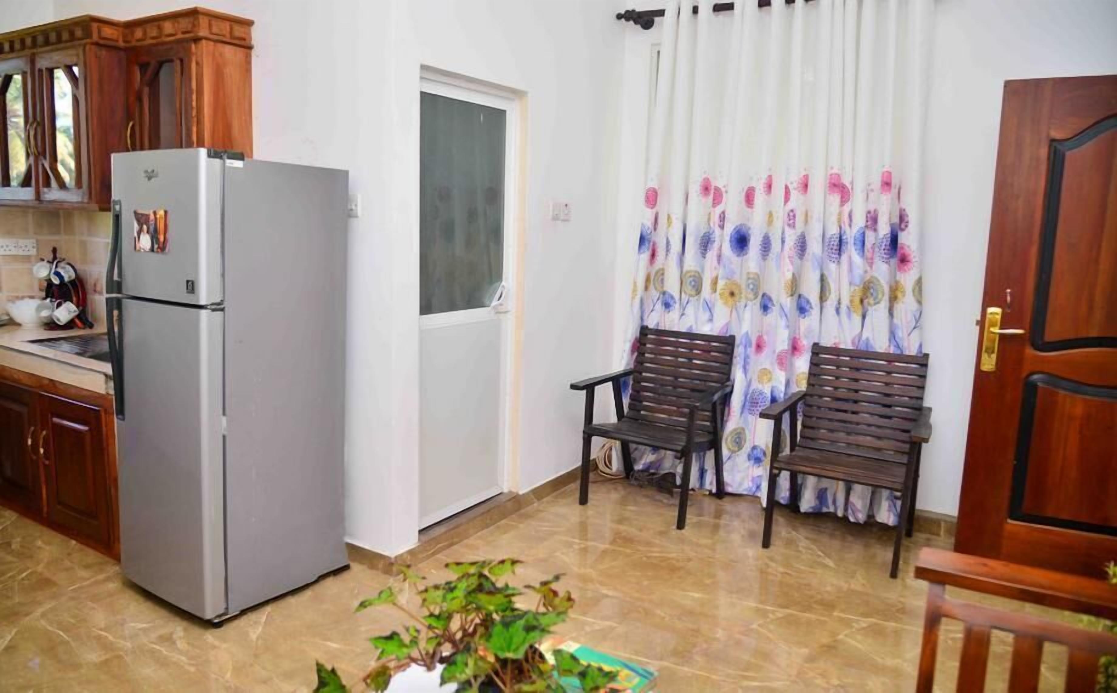 A compact kitchen with a refrigerator, wooden cabinets, and a window with curtains.