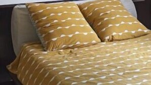 Une chambre à coucher avec un lit, deux oreillers, une œuvre d’art accrochée au mur et un luminaire au plafond.
