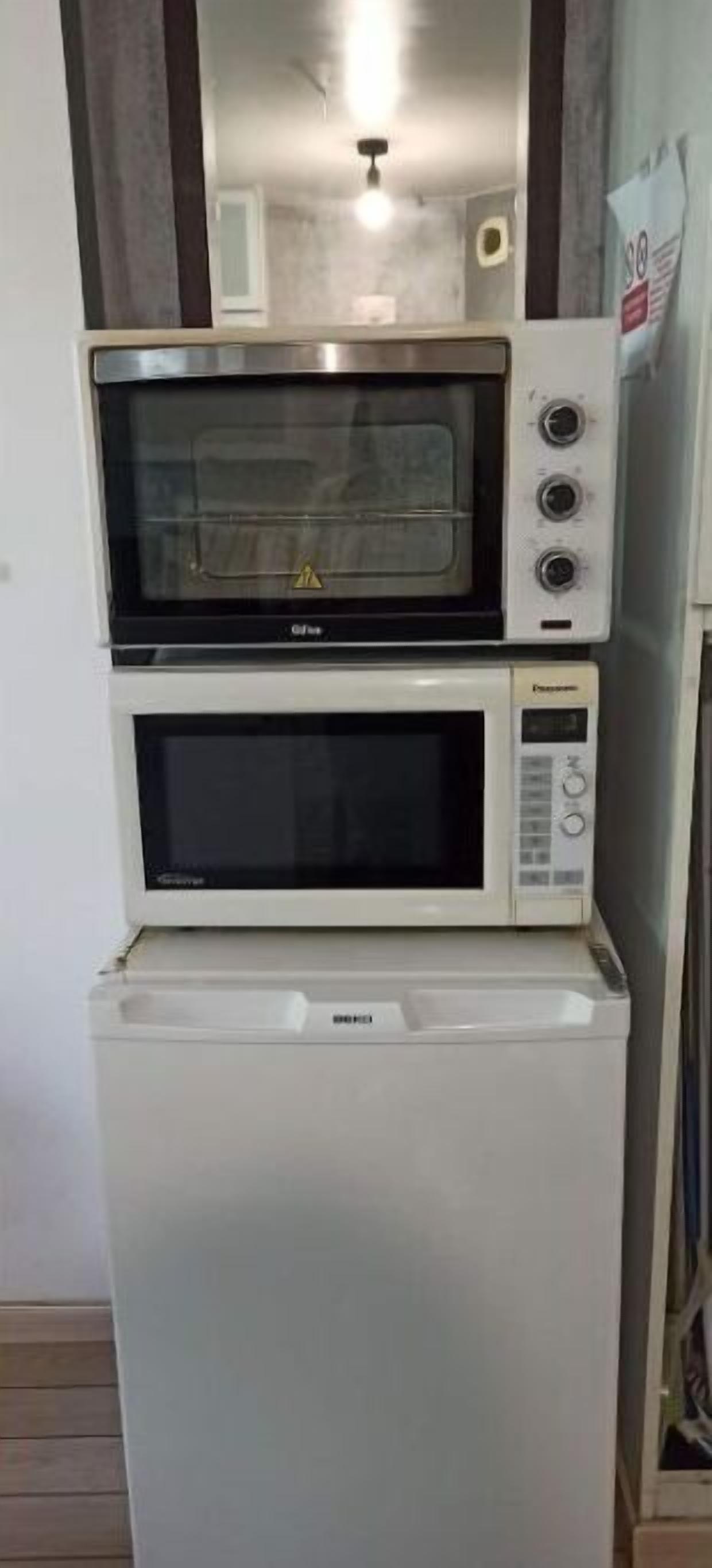 A compact kitchen with a built-in microwave and oven, a white refrigerator, and a wooden cabinet.
