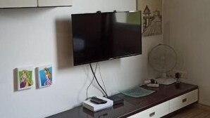 Un salon moderne avec un téléviseur à écran plat fixé au mur, un meuble en bois doté de tiroirs et une petite étagère ornée d’objets décoratifs.