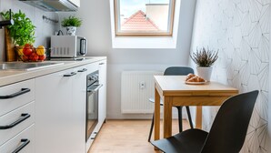 A compact kitchen with white cabinets, a microwave, a small table with a chair, and a window with a view of a building. - LeoApart (Wroclaw)