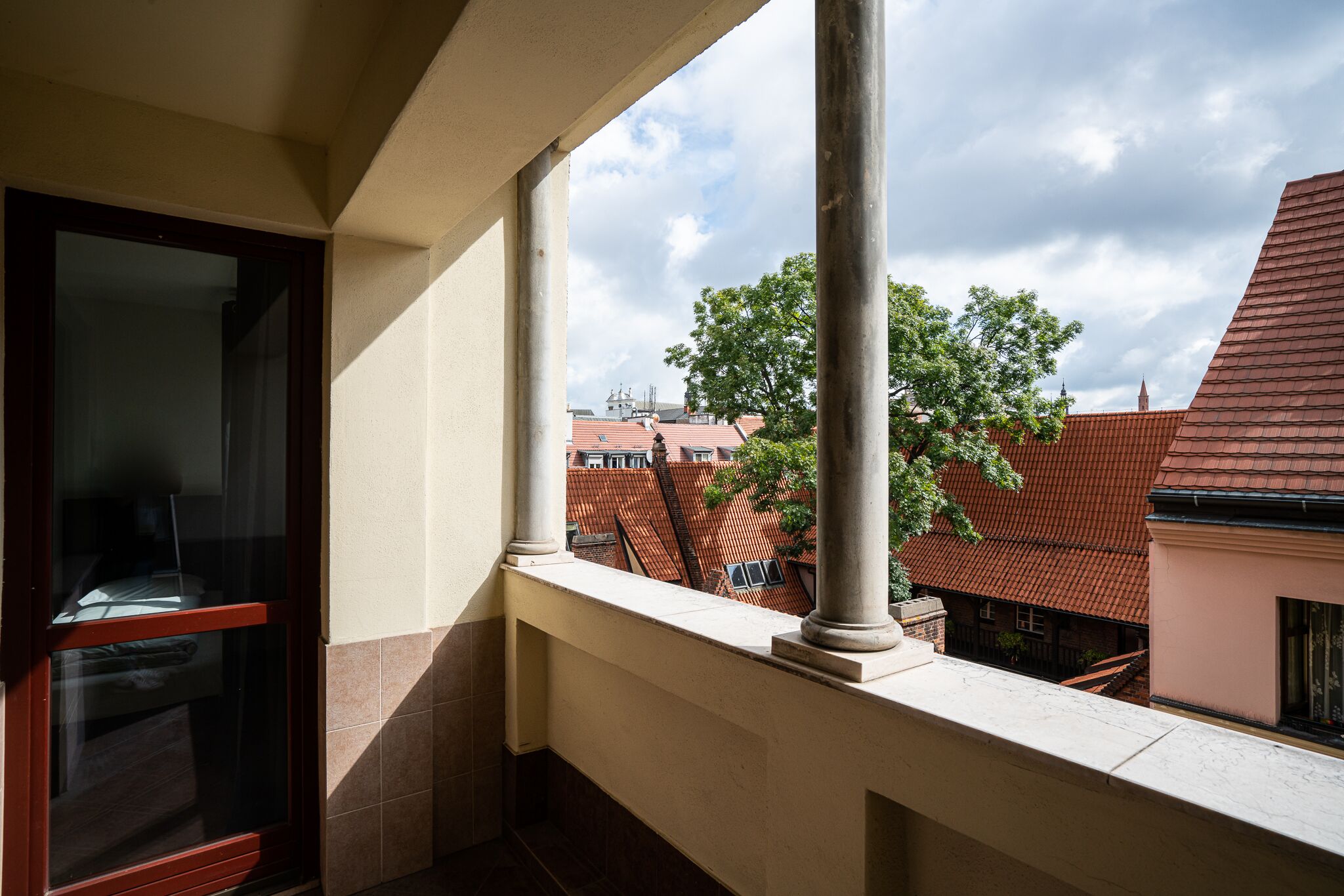 A balcony with a view of red-roofed buildings and a tree.