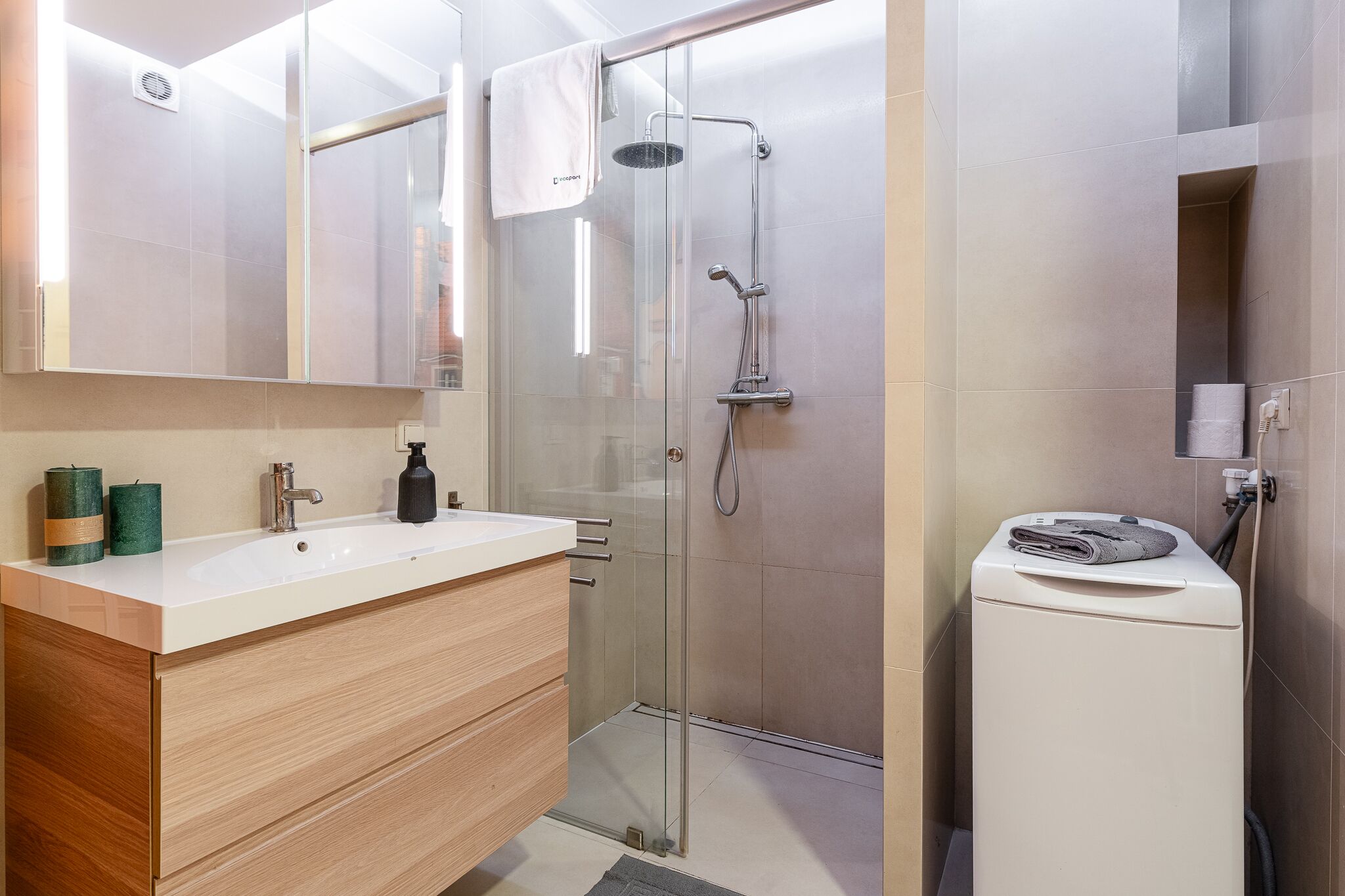 A modern bathroom with a glass-enclosed shower, a white sink with a wooden vanity, and a built-in washing machine.