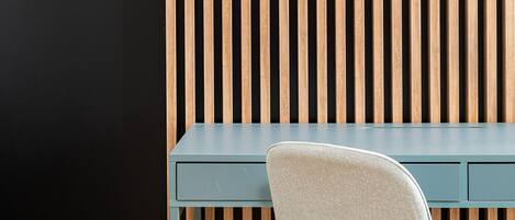 Una silla de oficina moderna con asiento y respaldo de tela gris claro, ubicada frente a un escritorio azul oscuro sobre un fondo de listones de madera verticales.