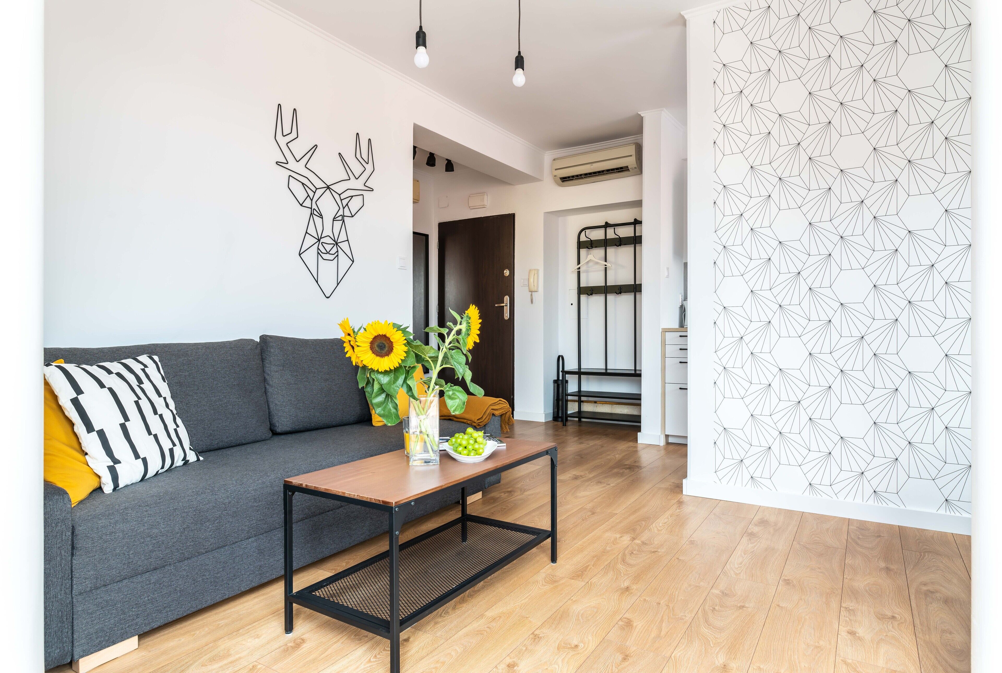Een moderne woonkamer met een grijze bank, een houten salontafel en een aan de muur bevestigde decoratie van een hertenkop.