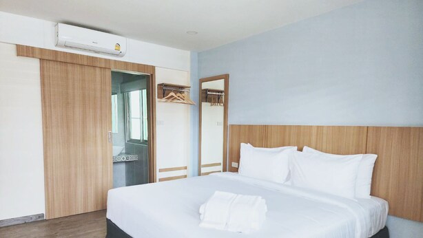 A hotel room with a large bed, a wooden wardrobe, a mirror, and an air conditioning unit.