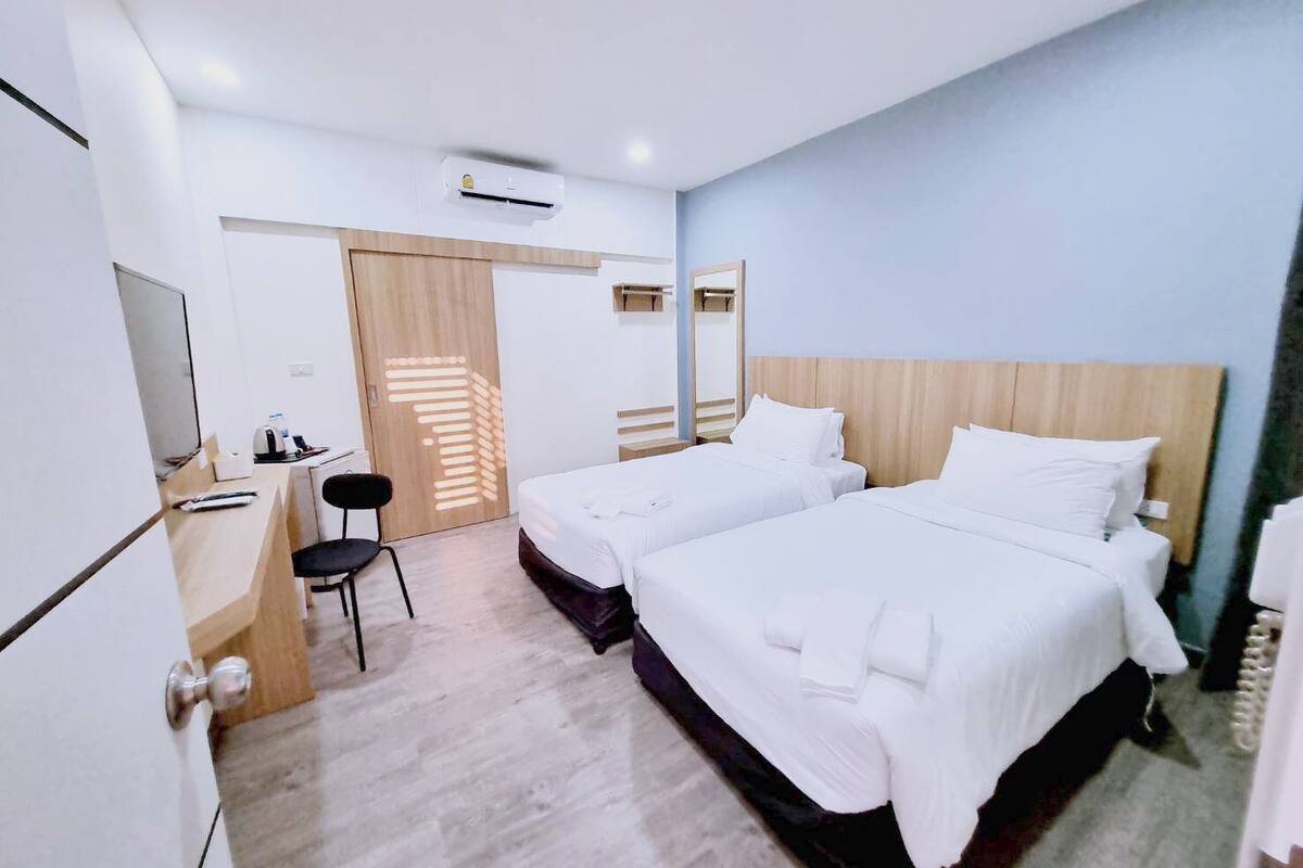 A hotel room with two beds, a desk, a chair, and a wardrobe.