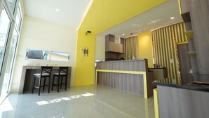 A modern kitchen with a yellow accent wall, a bar area with stools, and a large window providing natural light.
